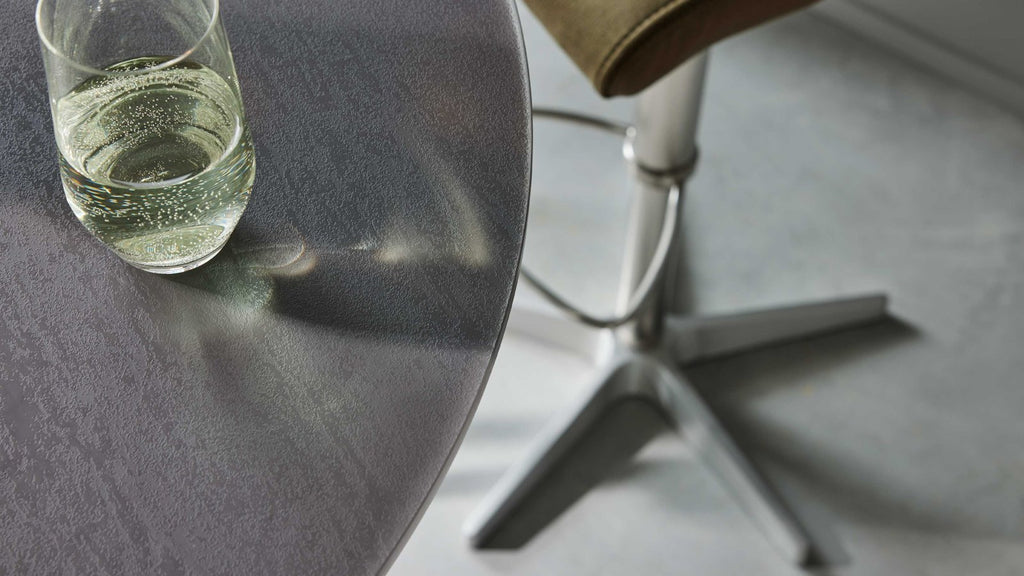 Bartisch mit runder, dunkelgrauer Platte und modernem Edelstahlgestell